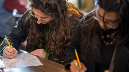 Two young women concentrating hard while writing in a workshop